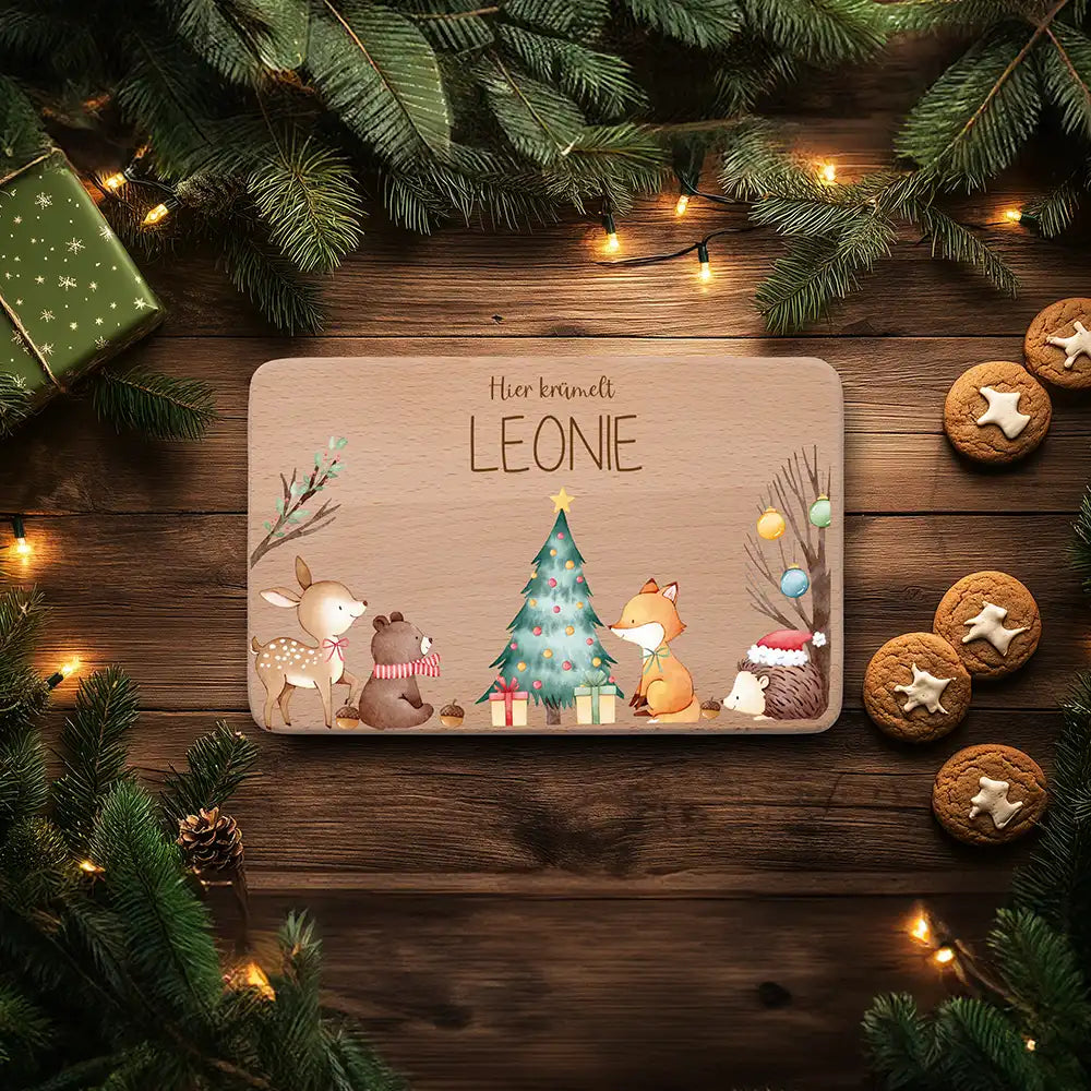 Frühstücksbrettchen mit dem Namen Leonie und Waldtieren um einen Weihnachtsbaum, daneben Tannenzweige und Lebkuchen
